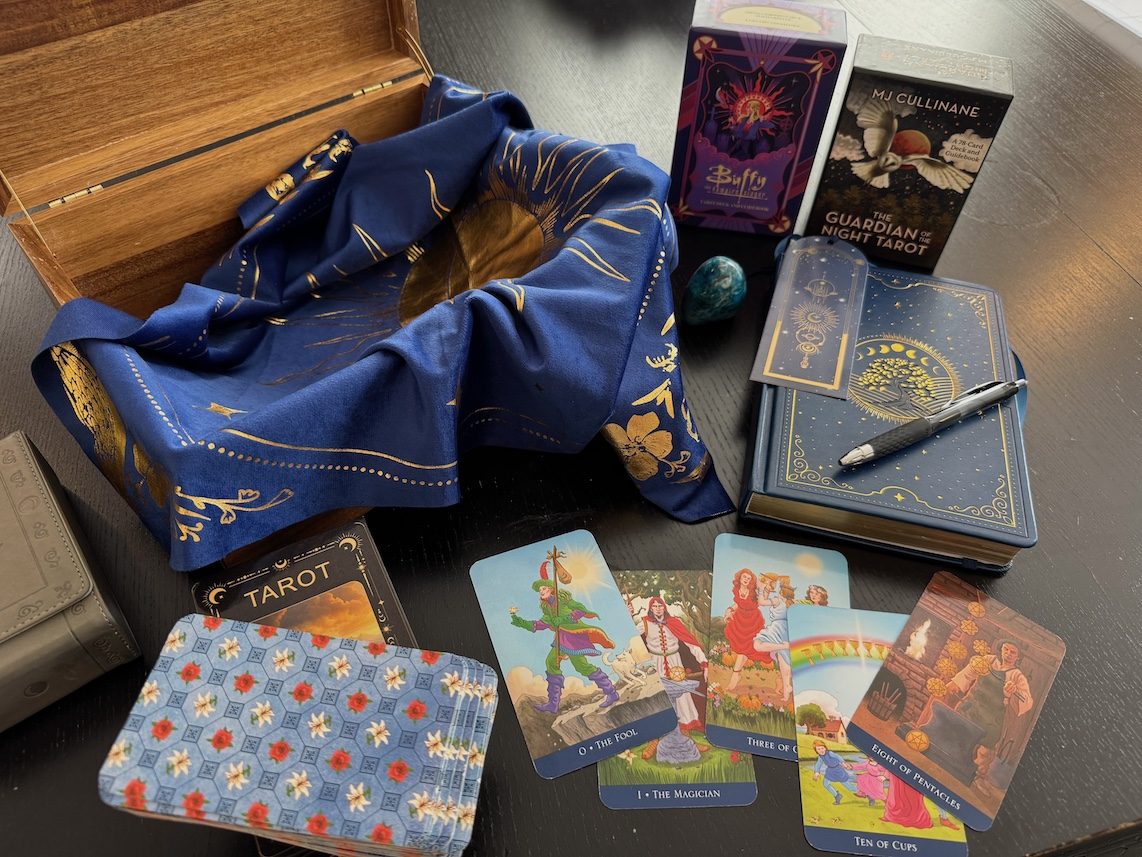 Tarot cards spread across a royal blue and gold cloth, with decks and my logbook